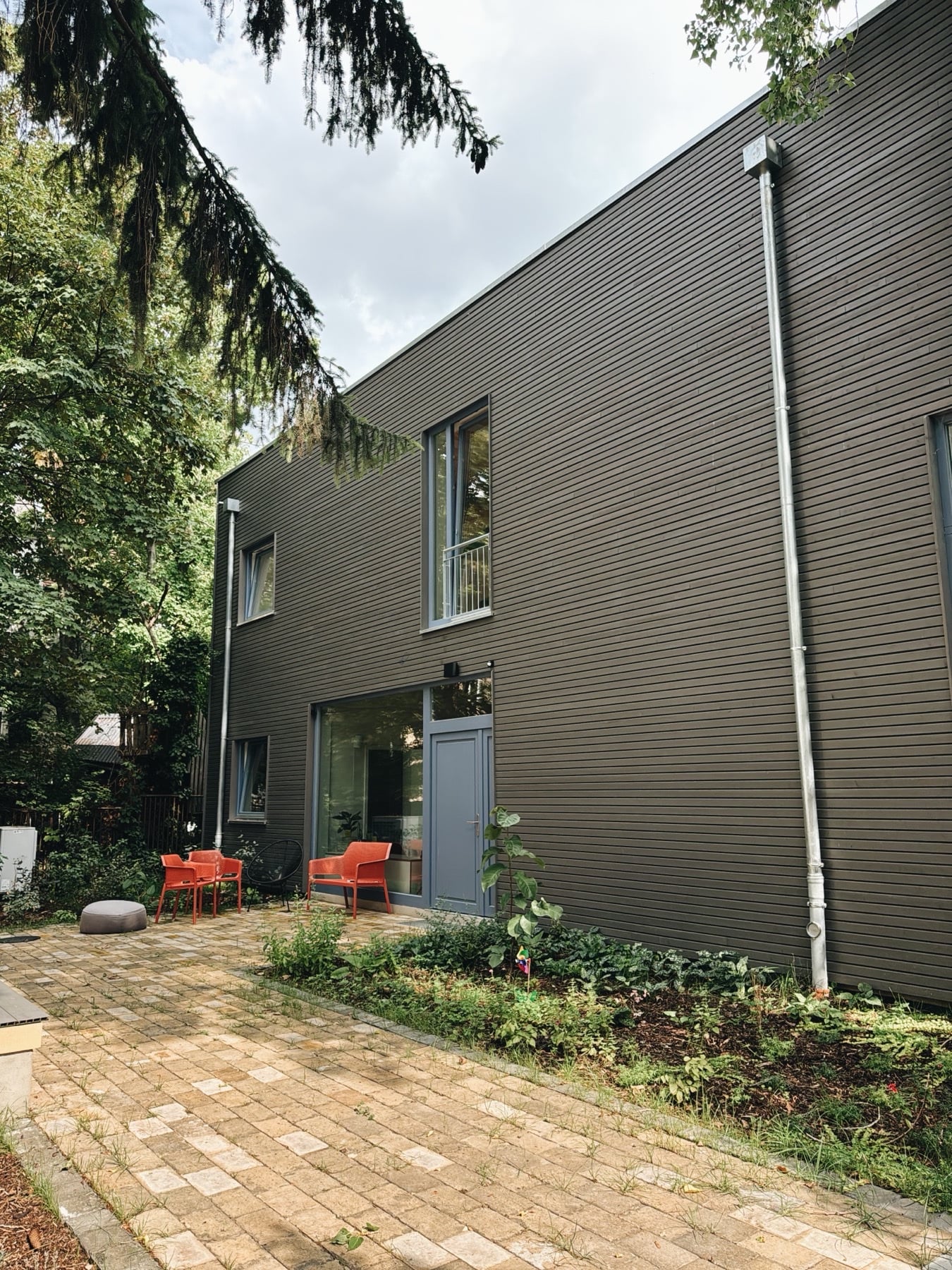 Der Hinterhof: Holzfassade, blaue Tür, orange Stühle unter dem Baum