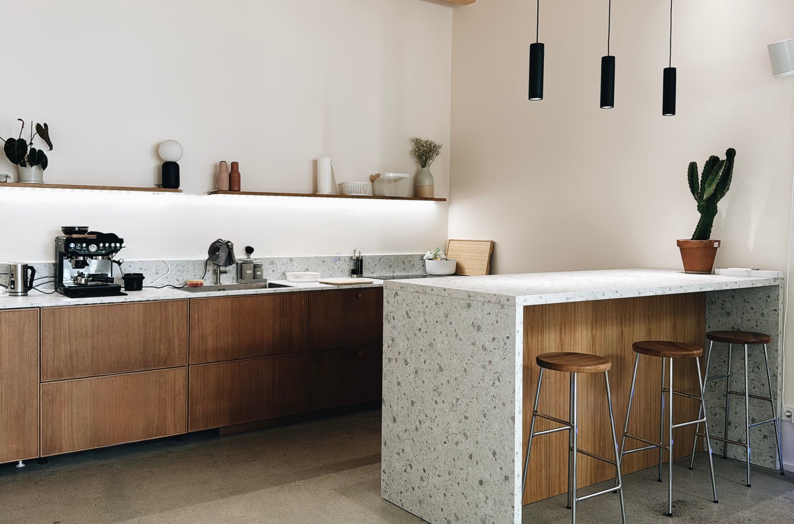 Die Küche: Terrazzo-Theke, Holzfronten, Siebträger, drei Barhocker